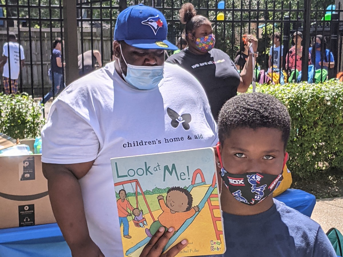 A Children's Home & Aid staff member and a young reader with a picture book at a community book giveaway